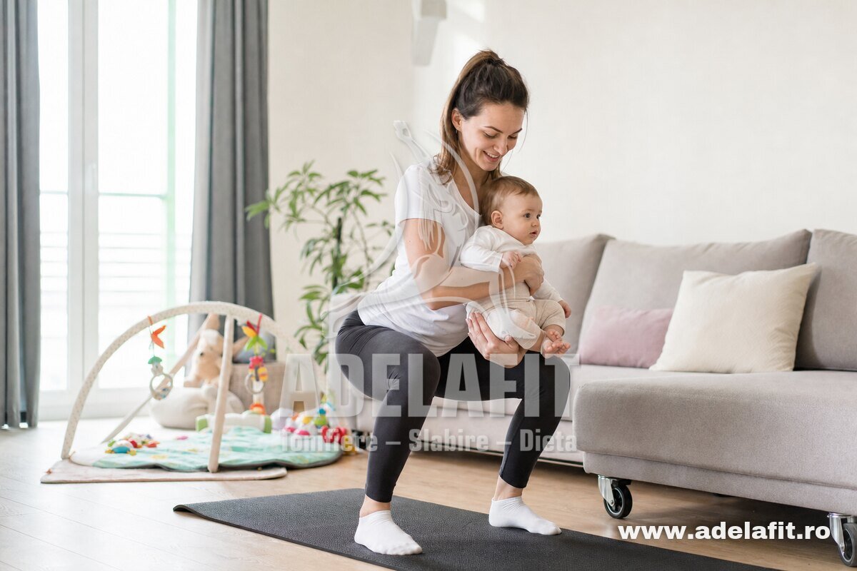 Mamă făcând genuflexiuni cu bebelușul în brațe în sufragerie luminoasă