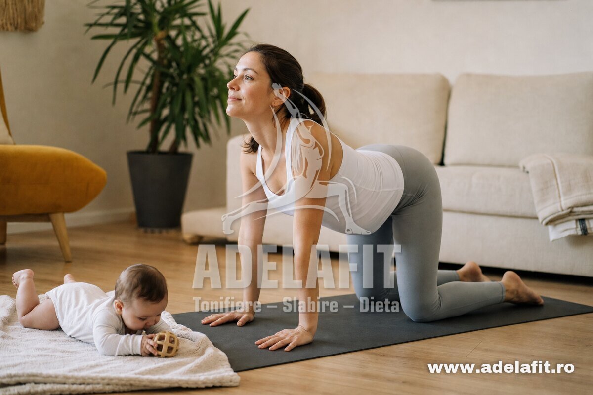 Mamă tânără face exercițiul pisica-vaca pe covoraș, bebelușul stă lângă ea pe pătură.