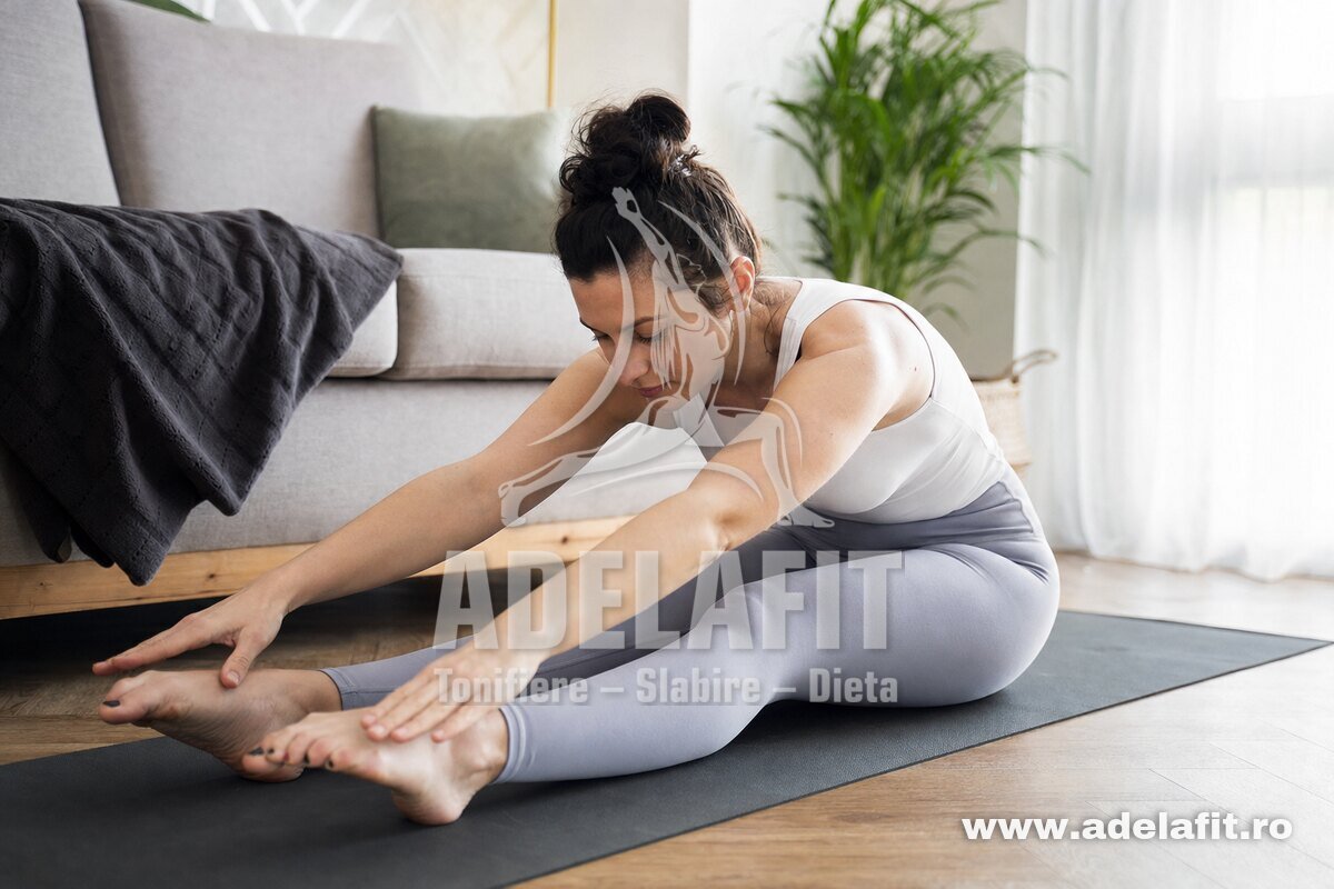 Femeie făcând exercițiul Spine Stretch Pilates pe saltea, acasă, într-un living luminos