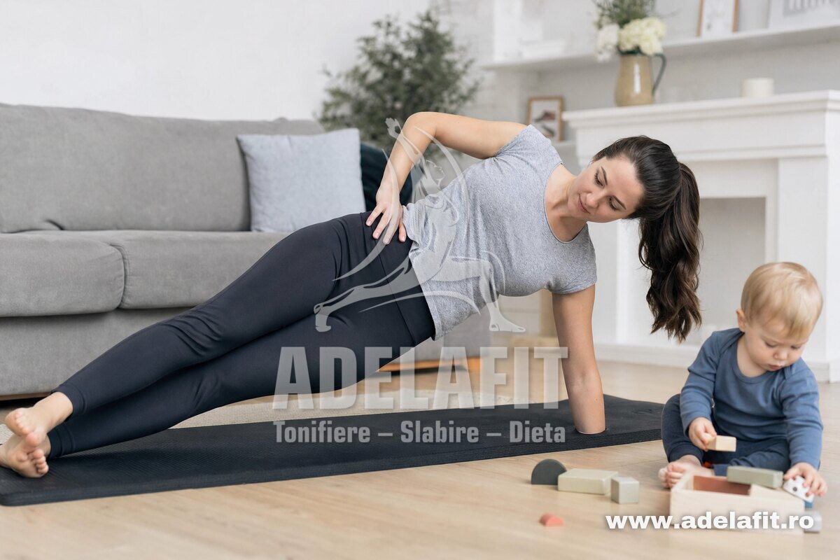 Mamă făcând plank lateral acasă, copil mic jucându-se lângă ea pe covor