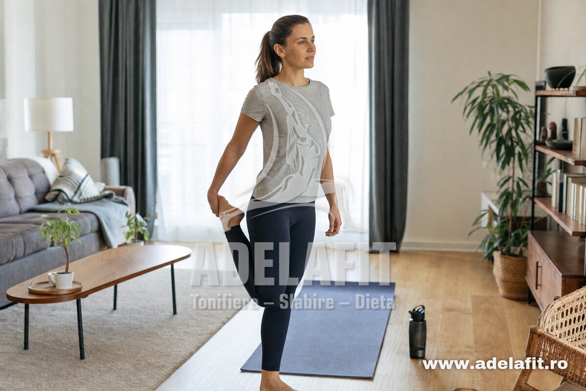 Femeie făcând stretching dimineața acasă, întinzând coapsa, în echipament sport simplu